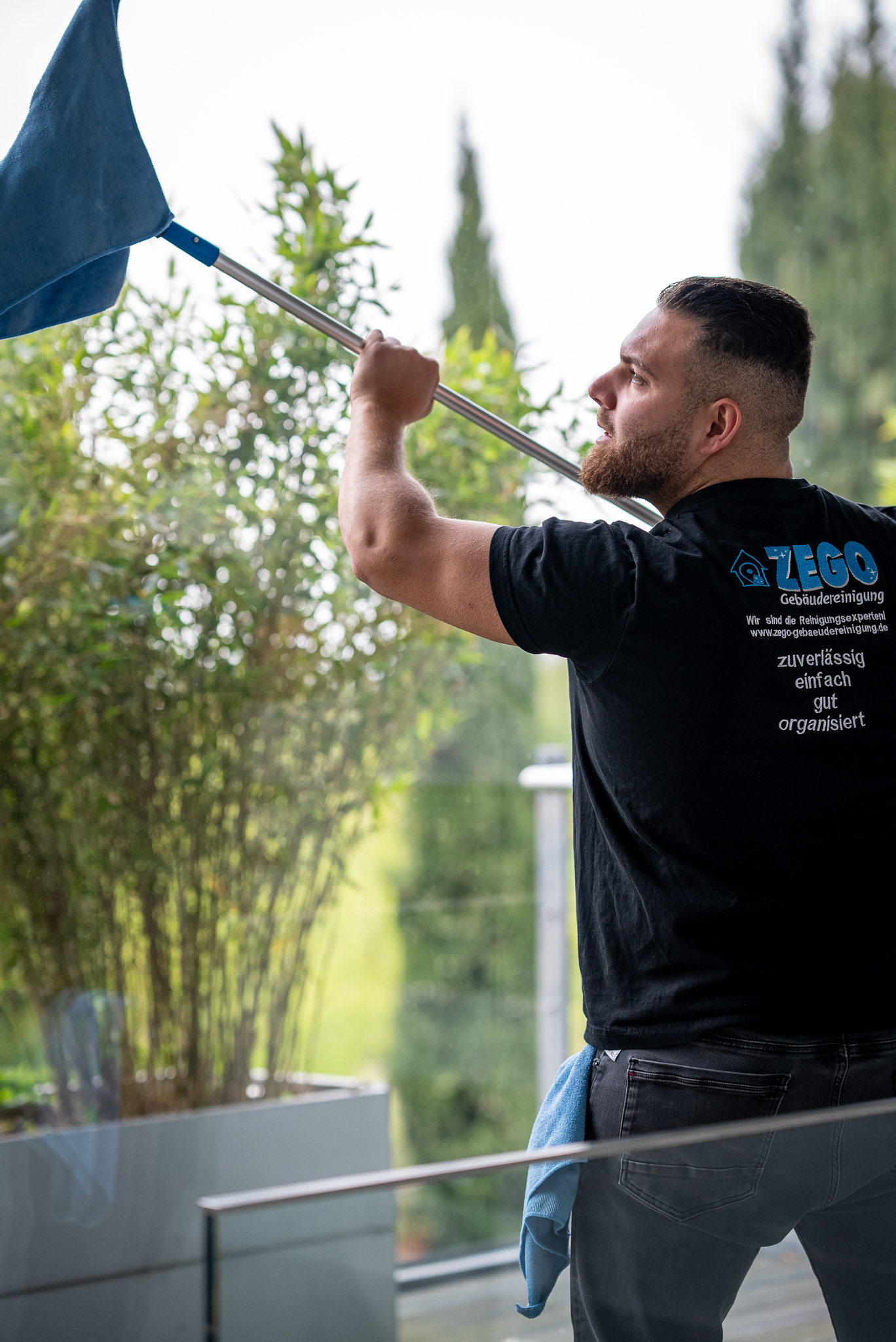 Mitarbeiter von ZEGO reinigt mit der Teleskopstange die Glasflächen einer Terrasse