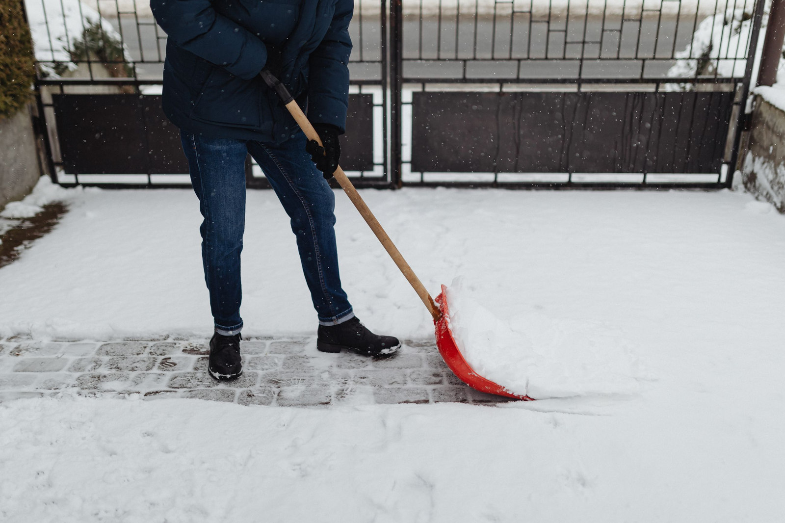 Person räumt mit einer Schneeschaufel einen gepflasterten Weg